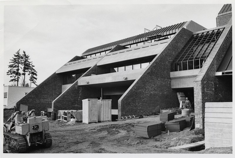 Black and white photograph of sloping metal and brick exterior of CDRC, set against unfinished dirt roads and construction equipment.