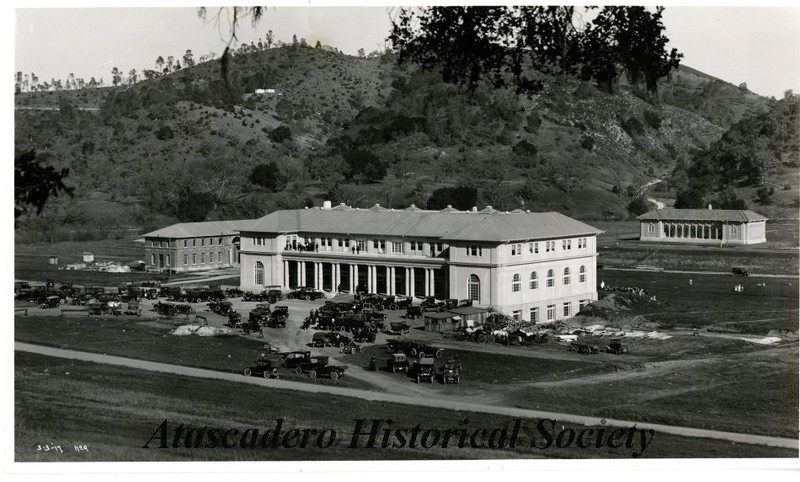 B&W photo showing the La Plaza (Atascadero Inn) with many cars parked in front. The Printery can be seen at left and the elementary school at right background. Ca 1917