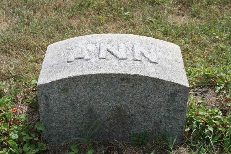 A simple stone marker with a curved top and the name "Ann" in raised letters on the top.