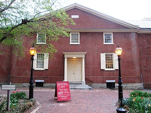 Brick building with two columns flanking entrance. A tree stands between the viewer and the building.