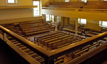 Elevated view of interior,  taken from the balcony of the meeting house, with pews on the floor and on risers below.