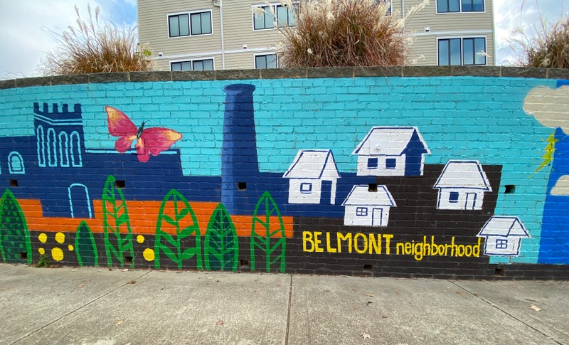 Bright, colorful, images of the neighborhood are painted with a blue background on a retaining wall.