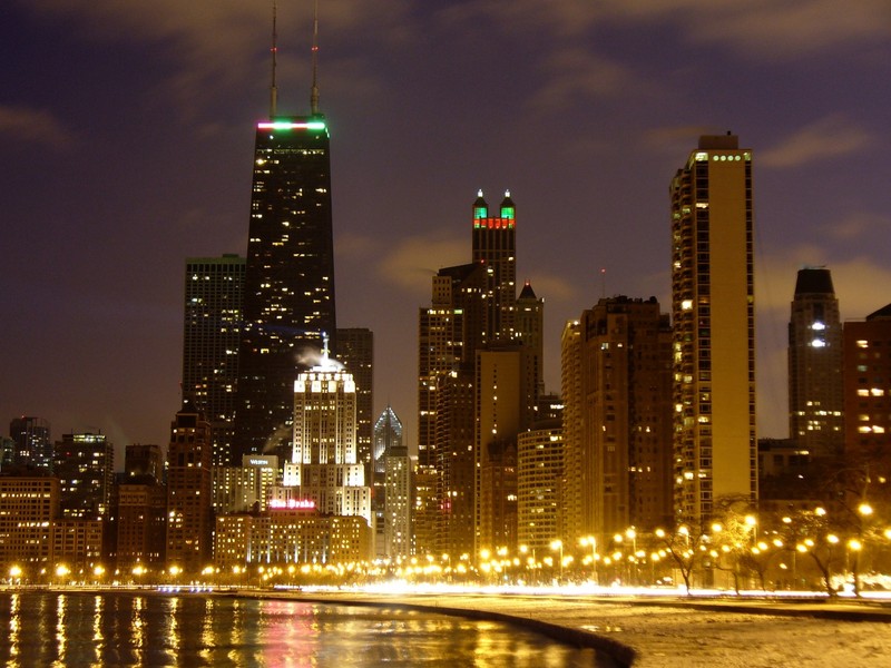 Oak Street Beach View: This is a photograph of Oak Street Beach in Chicago, IL on a cold night in January. The road in this picture is Lake Shore Drive. The bright, art deco building with the lit beacon is the Palmolive Building.