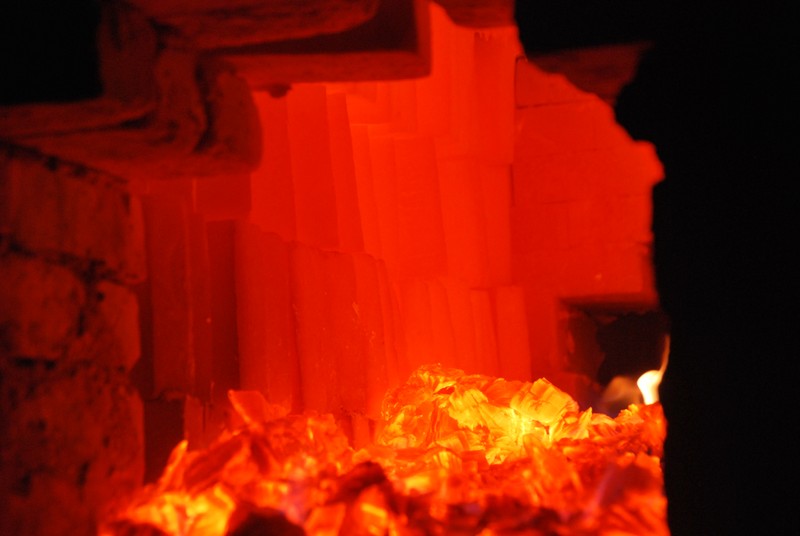 Image of the inside of the kiln, showing stacks of red-hot bricks behind a pile of glowing coals.