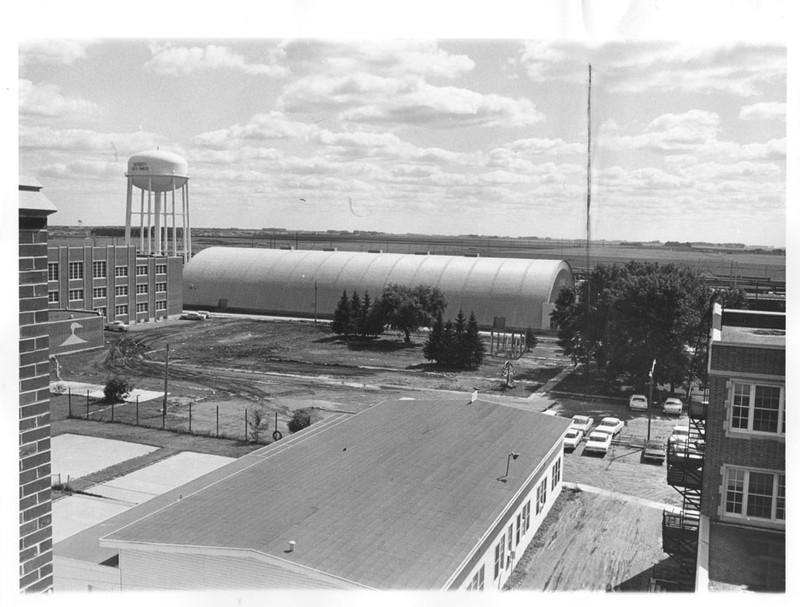 Quonset hut known as "the Barn" seen in the distance from above; roof of other building in the foreground.
