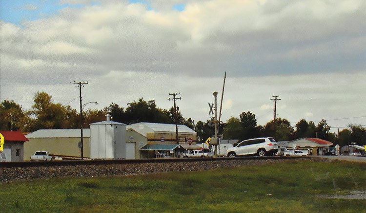 A colored photo of a car going across some tracks into a town.