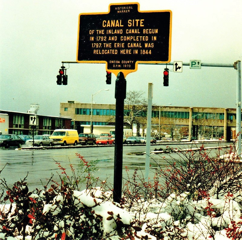 This shows the marker as it was in the 1970s with the now demolished "Living Bridge," an overhead walkway that once provided pedestrians a route over Erie Blvd., in the background, Image courtesy of Rome Historical Society.