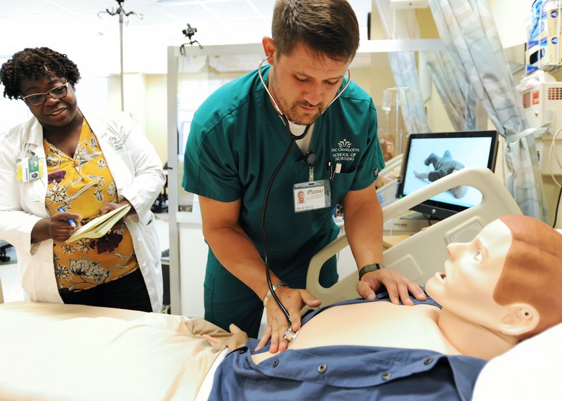 Male student using a stethoscope on a medical mannequin