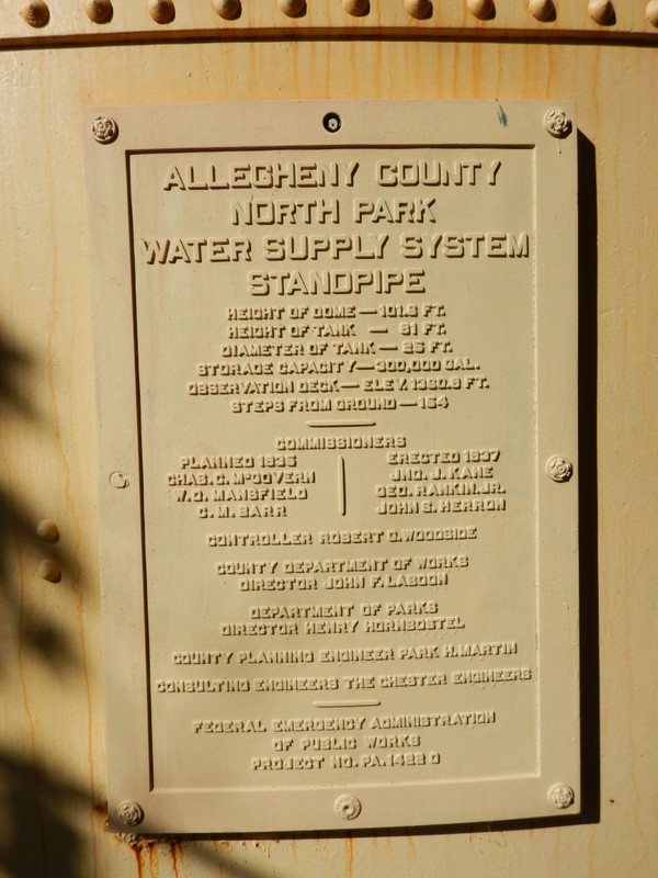 A yellow rectangular plate is engraved with the following text: ALLEGHENY COUNTY NORTH PARK WATER SUPPLY SYSTEM STANDPIPE HEIGHT OF DOME – 101.6 FT. HEIGHT OF TANK – 81 FT. DIAMETER OF TANK – 25 FT. STORAGE CAPACITY – 300,000 GAL. OBSERVATION DECK – ELEV. 1360.8 FT. STEPS FROM GROUND – 154   COMMISSIONERS: Planned 1935: Chas.C.McGovern, W.D.Mansfield, C.M. Barr. Commissioners: Erected 1937: JNO J. Kane, Geo. Rankin Jr., John S. Herron.         CONTROLLER ROBERT G. WOODSIDE  COUNTY DEPARTMENT OF WORKS DIRECTOR JOHN F. LABOON  DEPARTMENT OF PARKS DIRECTOR HENRY HORNBOSTEL  COUNTY PLANNING ENGINEER PARK H. MARTIN   FEDERAL EMERGENCY ADMINISTRATION OF PUBLIC WORKS PROJECT NO. PA. 1422 D