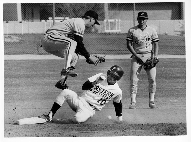 An Eastern baseball player sliding into base in a game against the University of Louisville.  1970s.  EKU Photograph Collection.