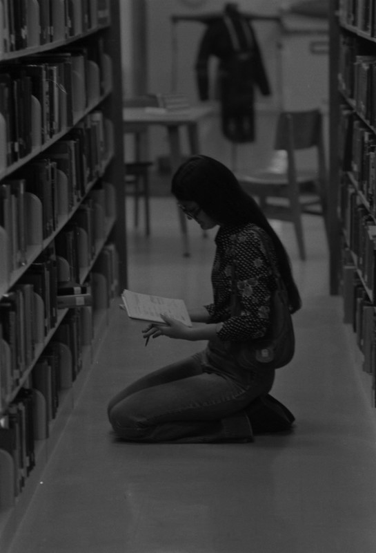 Student looking at a book in a book stack aisle, 1975. EKU Negatives Collection.