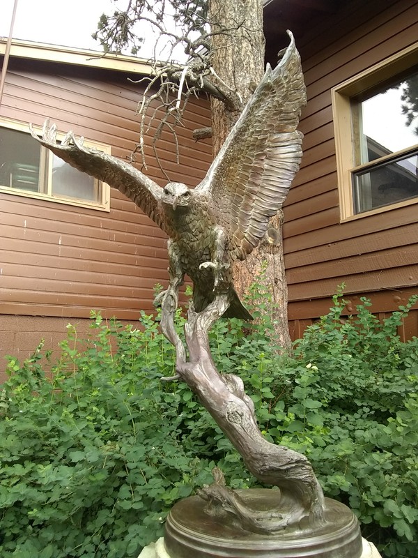 This sculpture is of a bronze eagle with its wings spread about to land on a curved branch. The eagle's left claws reach out as if to grab something. 