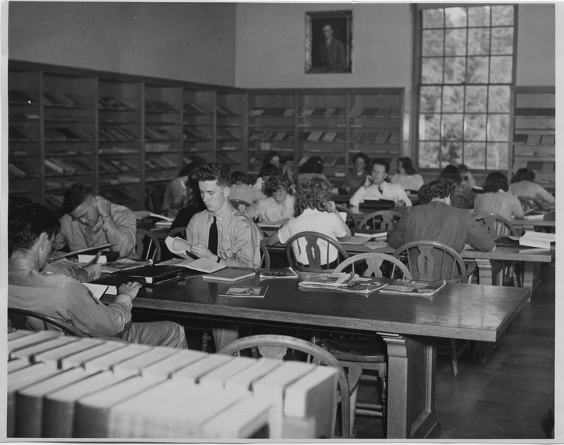 Black and white photograph of patrons at the Old Library engaged in research/reading at wooden tables surrounded by bookshelves.