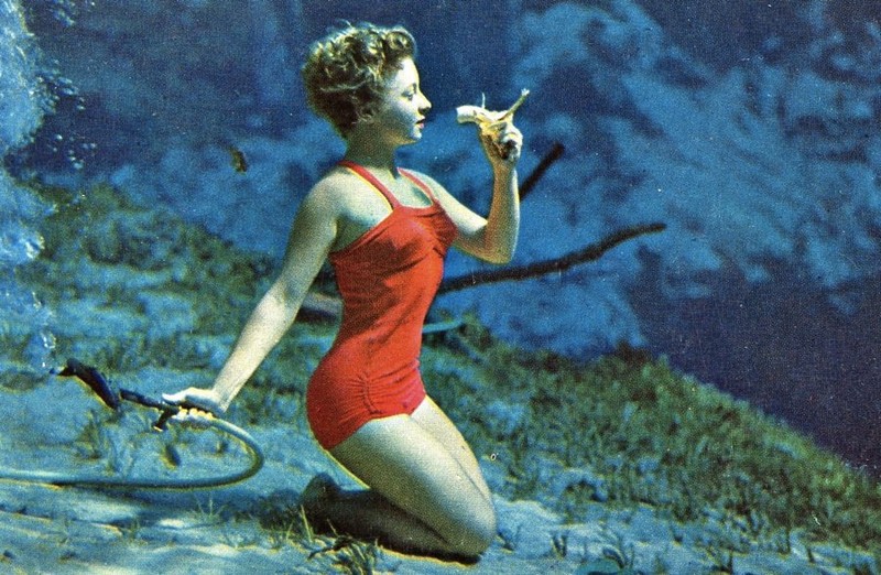 One of the early Weeki Wachee mermaids eating a banana underwater. This was one of the first things that the Weeki Wachee mermaids learned to do underwater. In her right hand is a free-flowing air hose that all the mermaids learn to breathe from.