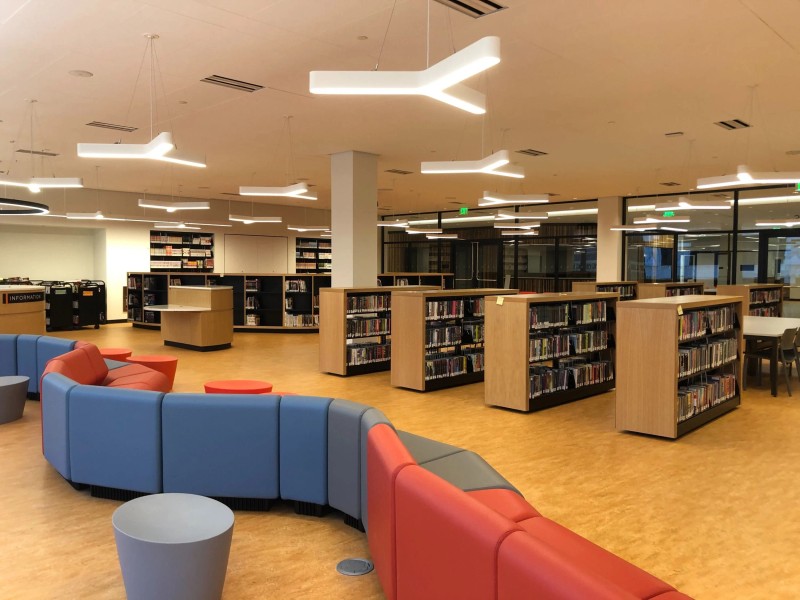 Interior photograph of the Alma Thomas Teen Center at the Martin Luther King Jr. Memorial Library, which pictures colorful curved seating area in the foreground, oak colored floor, and shelving full of books and a glass wall in the background.