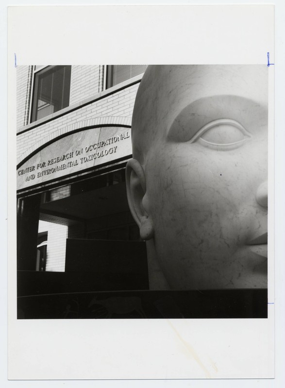 Black and white photograph of the entrance to the CROET (Center for Research on Occupational and Environmental Toxicology) with the half head sculpture, Vita Mensae, by artist Larry Kirkland, in the foreground.