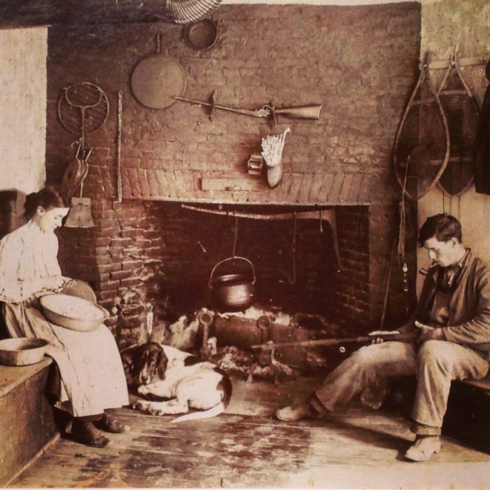 "Rowlie" and Mary Robinson, with a canine friend, at work in front of the old kitchen's hearth in the early 1900s.