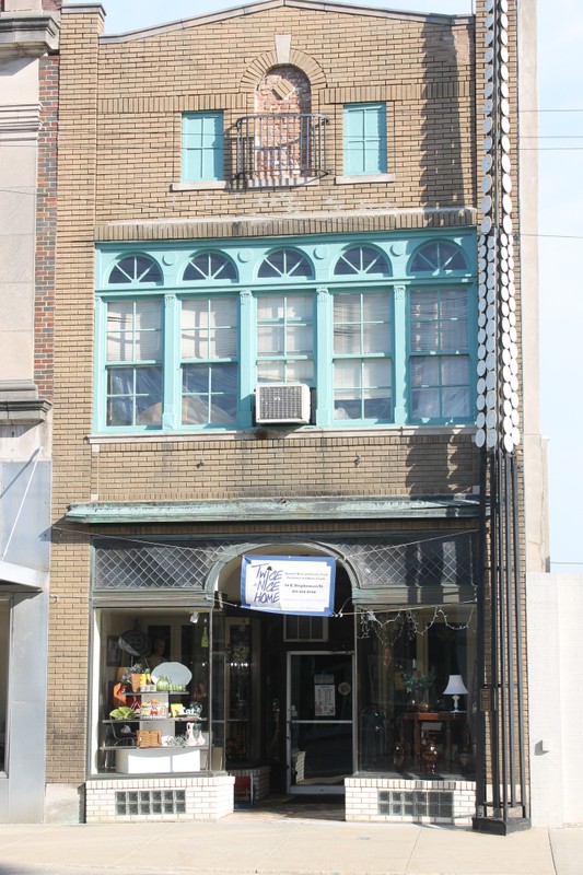 The front of a three story building built with sand-colored brick. The windows have cyan colored frames, and a sign on eht e first floor reads "Twice As Nice Home"