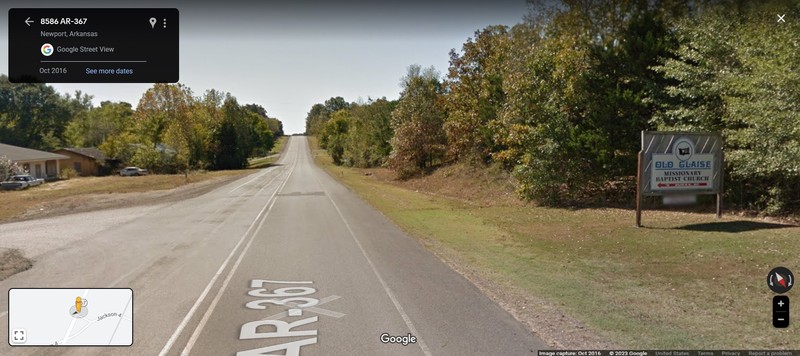 A colored photo with a paved road, entrance onto another road, and a sign.