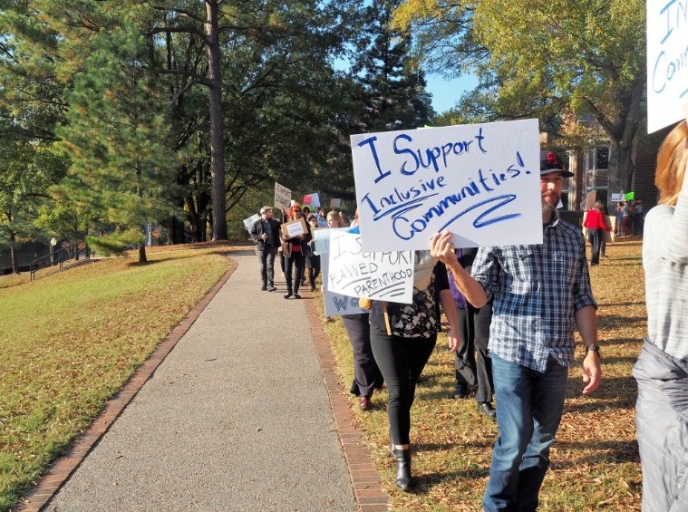 Professors and students gathering on the lawn outside of the library to protest injustices and fight for their beliefs: inclusivity of all communities.