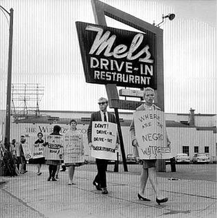 Protesters carry signs asking "Where are the Negro waitresses?" and encouraging would-be patrons to "drive out" instead of "drive in."