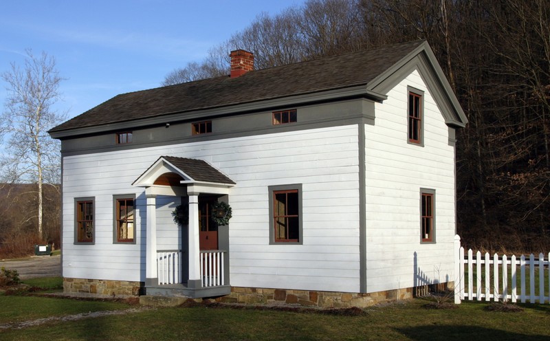 A simple, rectangular house, painted white. It has an old design, but looks newly built. 