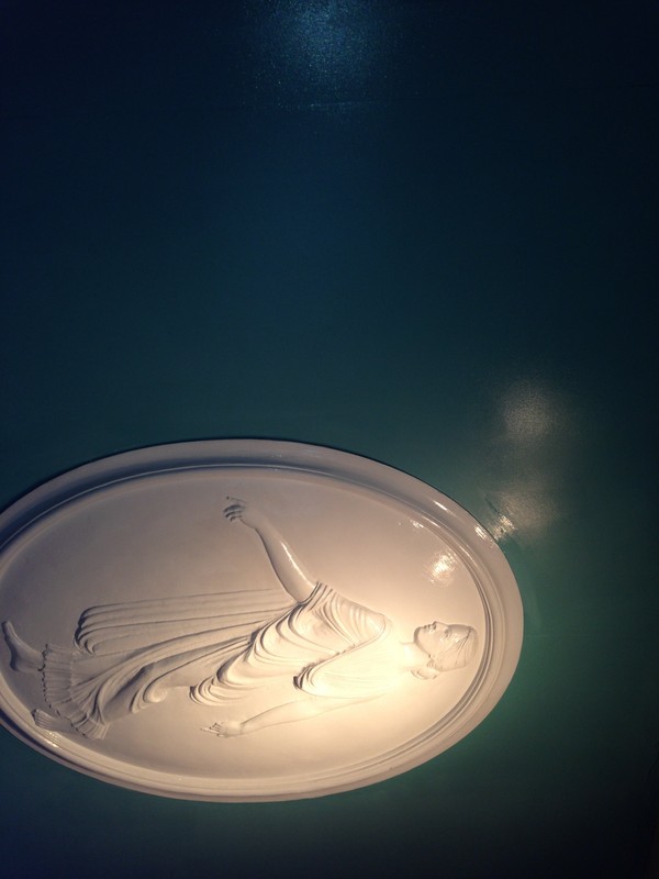 An original plaster Cameo relief on a wall that is flanked with neon lighting.