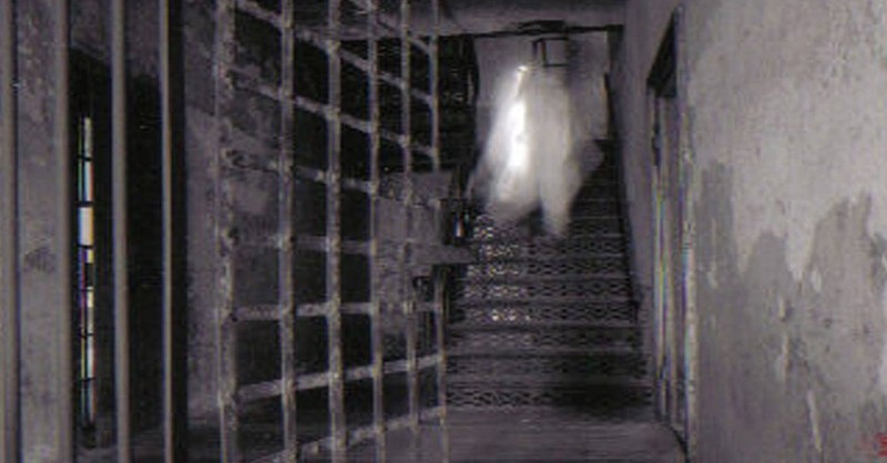 A photo captured of an open rusted cell door by a staircase of what appears to be the ghost of Lavinia Fisher.