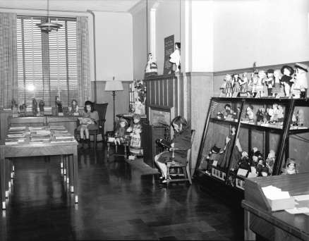 Two girls reading in the "Secret Room" for children in the Rundel Memorial Library. The George W. Cooper Doll Collection adorns the walls and shelves. (October 25, 1940)