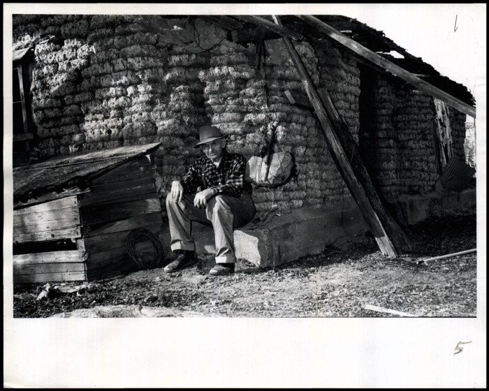 "Cherokee Strip Pioneer Marshall McCully suns himself at the corner of the old sod house he built when he settled the land in 1883."