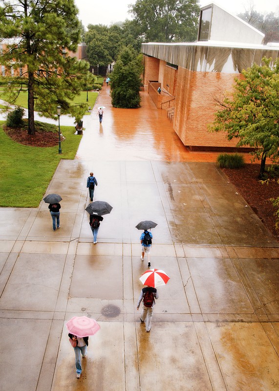 Rowe Arts Building in 2006 on a rainy day from a distance. The sidewalk outside of the building is in the foreground, with students walking with umbrellas.