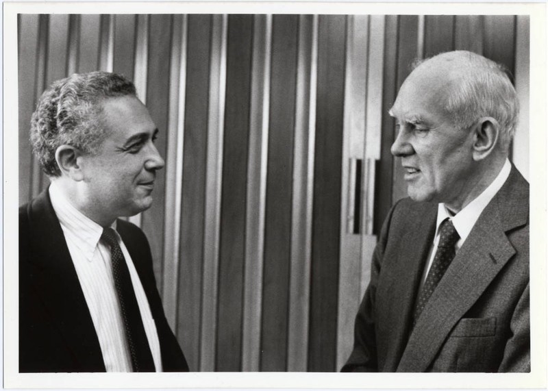 President Leonard Laster, M.D. stands in a suit in front of wooden doors, facing Howard Vollum, who also wears a suit.