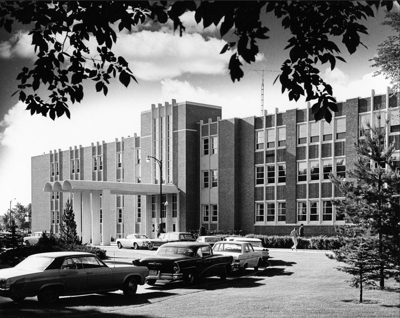 Black and white image of a large building with cars parked in front