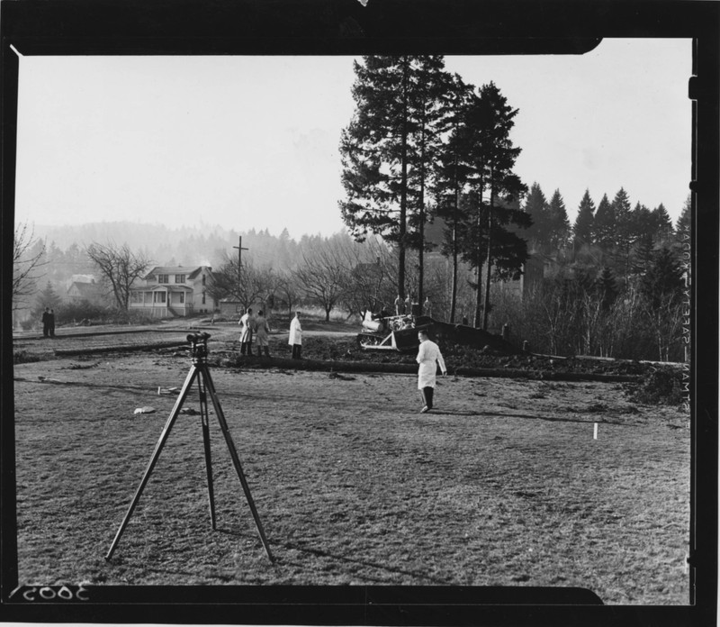 Black and white photograph of the future site of the Old Library and Auditorium. Includes view of men in physicians attire and surveyors equipment.