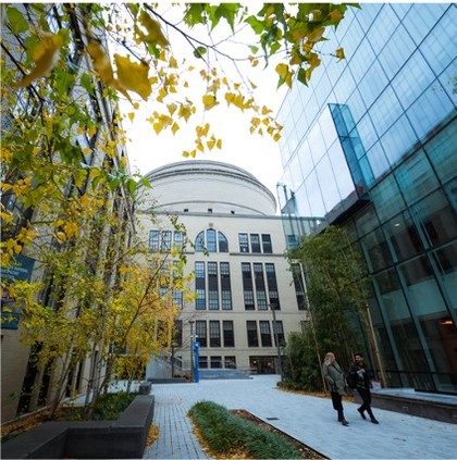 Courtyard surrounded by building walls. Pavement, trees. View of MIT Dome.