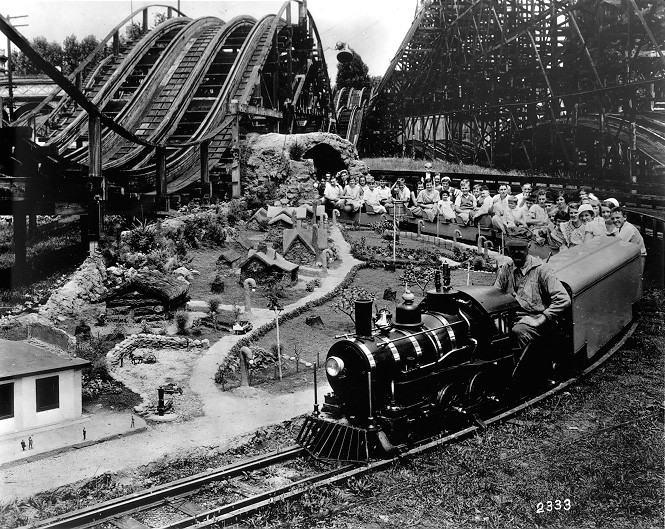 An image of the amusement park depicting a train with passengers in the foreground and part of the roller coaster in the background (black and white)