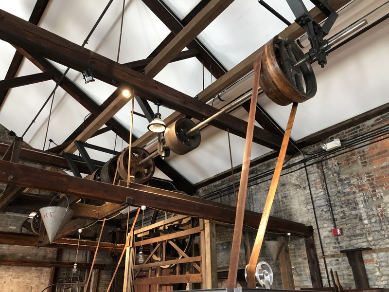 The lineshaft is attached to the ceiling and each machine is operated by a belt attached to wheels on the shaft.