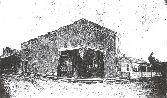 A black and white photo of a building with a woman standing in front of it.
