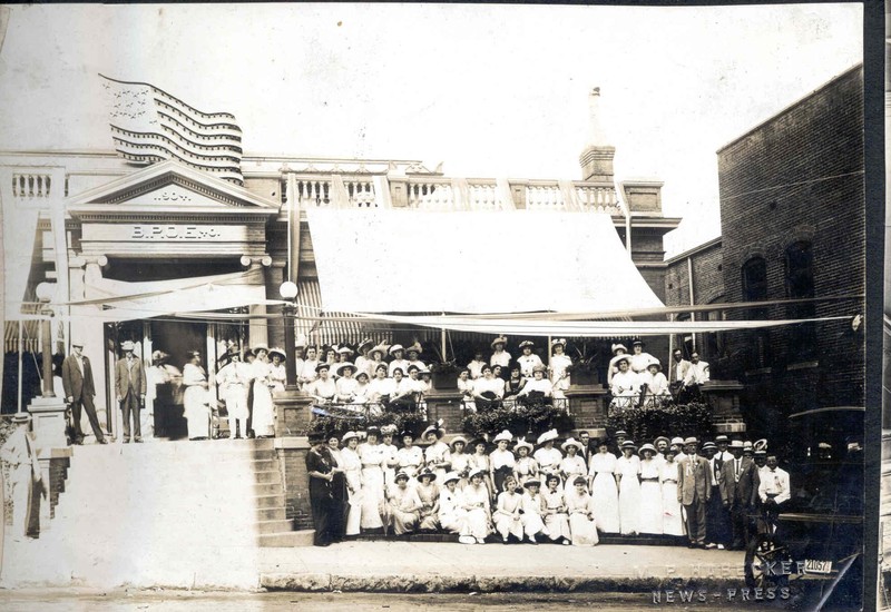 Elks Lodge Women's Group Photo, c. 1920s. b/w. A large group of women in white long dresses/hats posed on the sidewalk and porch of Elks Club Building, a few men in the photo. Image provided by the St. Joseph Museums, Inc.