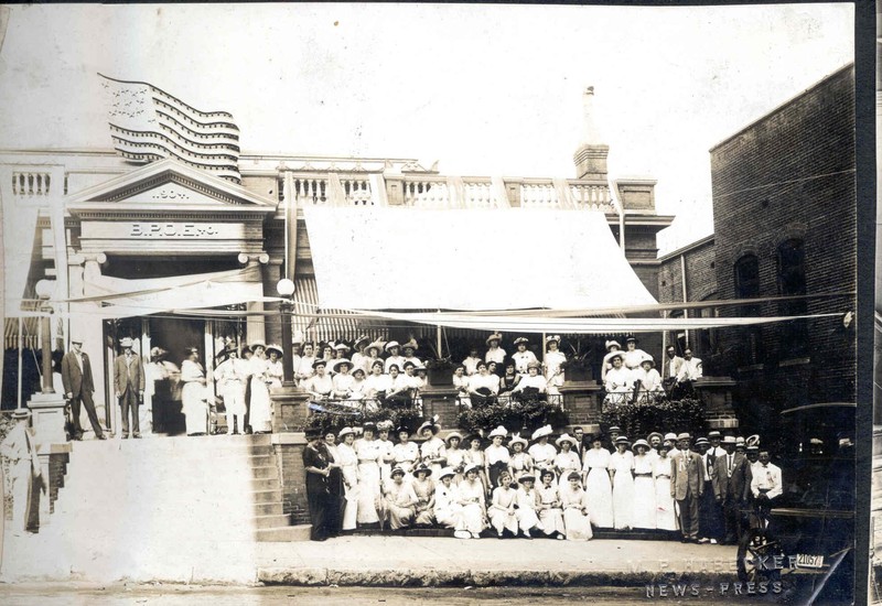 Elks Lodge Women's Group Photo, c. 1920s.  b/w.  A large group of women in white long dresses/hats posed on the sidewalk and porch of Elks Club Building, a few men in the photo.  Image provided by the St. Joseph Museums, Inc.