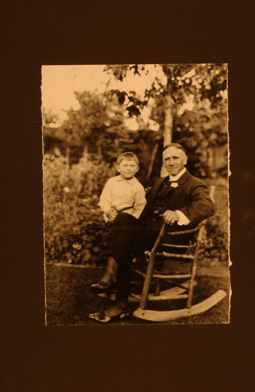 Black and white image of boy sitting on lap of man in rocking chair