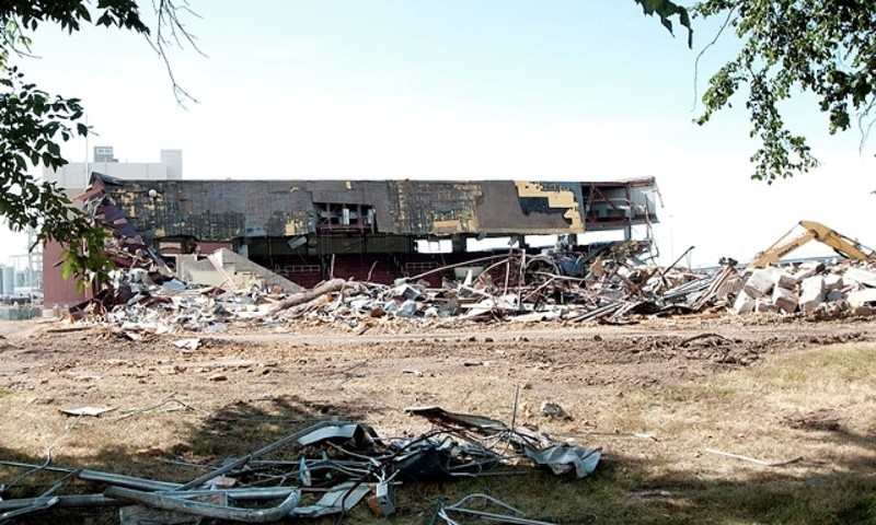 Dirt and scrap metal in the foreground; partially collapsed building in the distance.