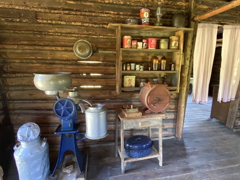 The interior of the cabin, showing a cream separator, a butter churner, and several shelves of foodstuffs
