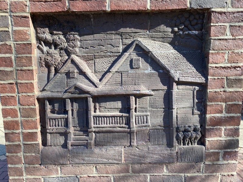 A tall brick sculpture stands in the middle of a small corner plaza.  Panels embedded in the brick are sculpture relief.