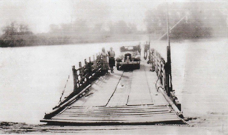 a black and white photo of a ferry crossing a river with a vehicle and people aboard.and o