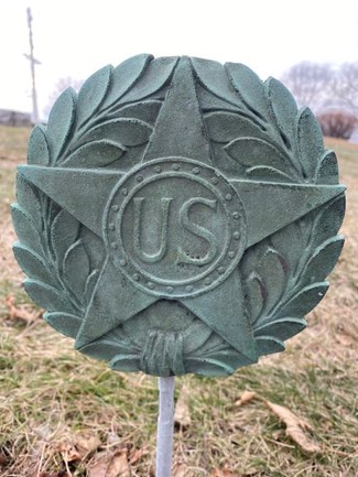 A green ceramic type material with a five-point star in the middle of a wreath, and inscribed in the star says "US" surrounded by a small circle of dots.