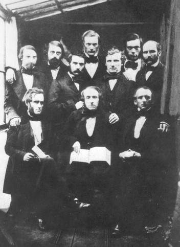 This is a black and white image of ten men at the first World Conference of YMCAs. Three are sitting in the front while the rest stand behind them. All the men are wearing dark suits with bowties.