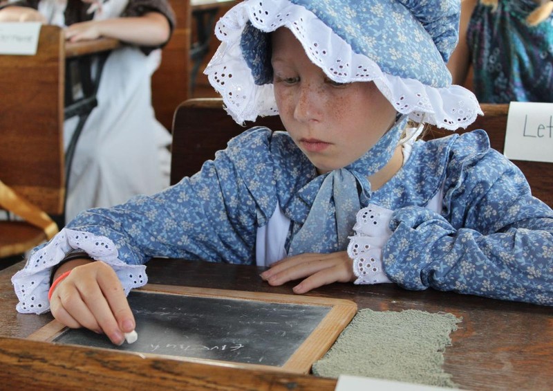 Student writing on slate at their desk during schoolhouse lesson