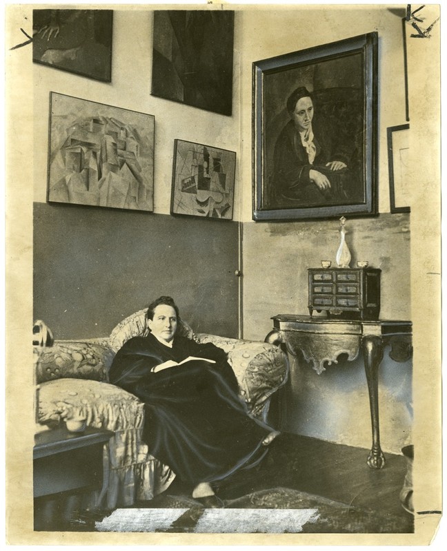 "Gertrude Stein sitting on a sofa in her Paris studio..."