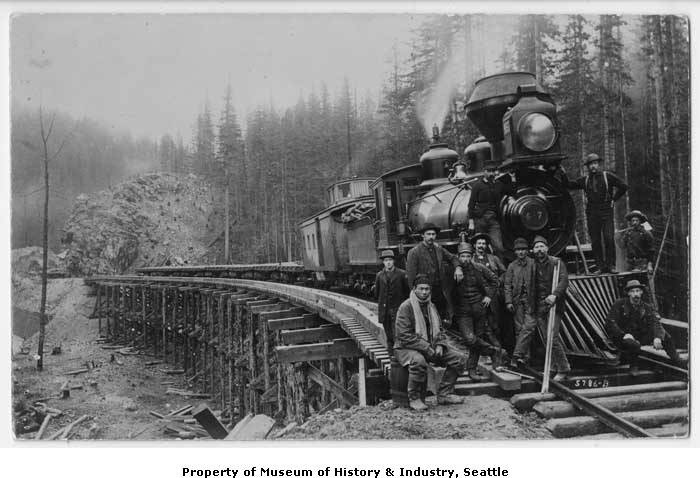 Group of construction workers posing in front of a Northern Pacific engine, #457, and caboose, at the Green River Crossing, 1885